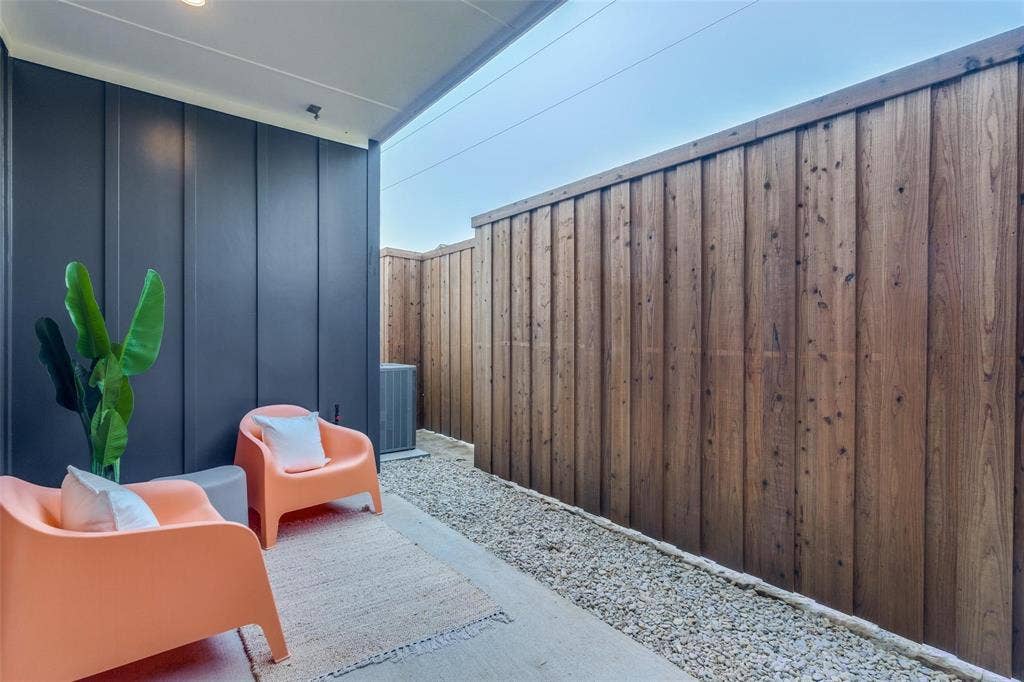Covered concrete patio featuring vertical charcoal-colored siding and a stained-wood board-on-board privacy fence, complemented by low-maintenance gravel landscaping