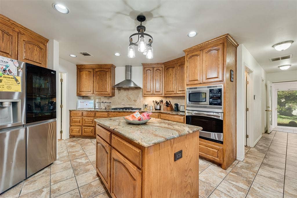 Kitchen featuring raised-panel oak cabinetry, stone countertops, central island, stainless steel appliance suite, and tile flooring
