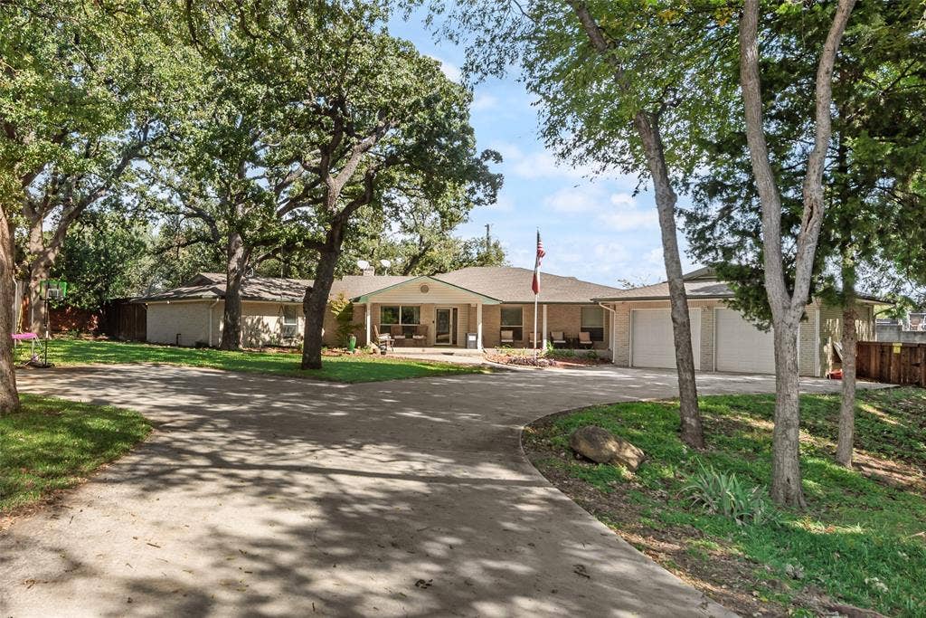 Single-story brick exterior featuring an expansive concrete driveway, attached two-car garage, covered entryway, and mature shade trees