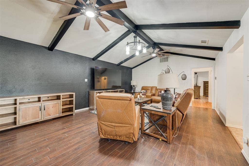 Vaulted ceiling featuring exposed dark-finish structural beams, wood-finish flooring, and dual ceiling fans