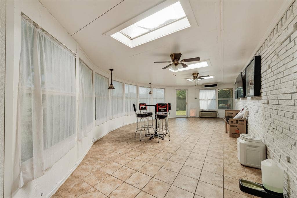 Sunroom featuring ceramic tile flooring, a painted brick accent wall, multiple skylights, and ceiling fan fixtures