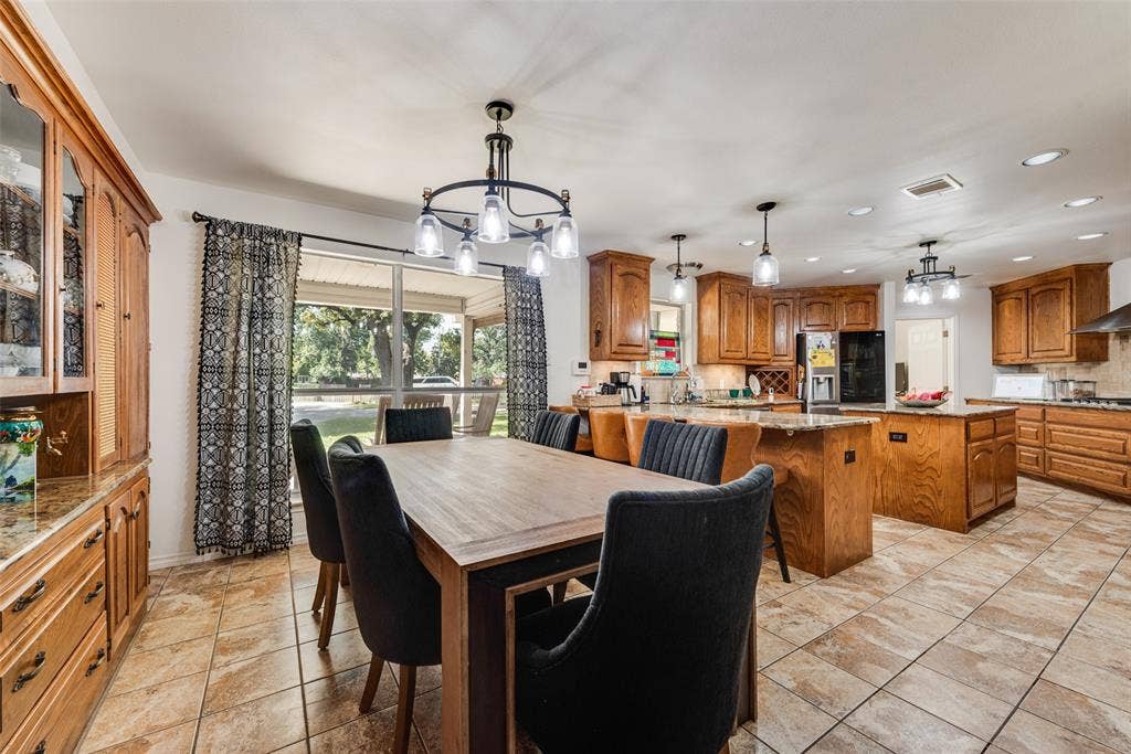 Kitchen featuring custom wood cabinetry, a center island with countertop seating, stone-finish tile flooring, and multiple pendant light fixtures