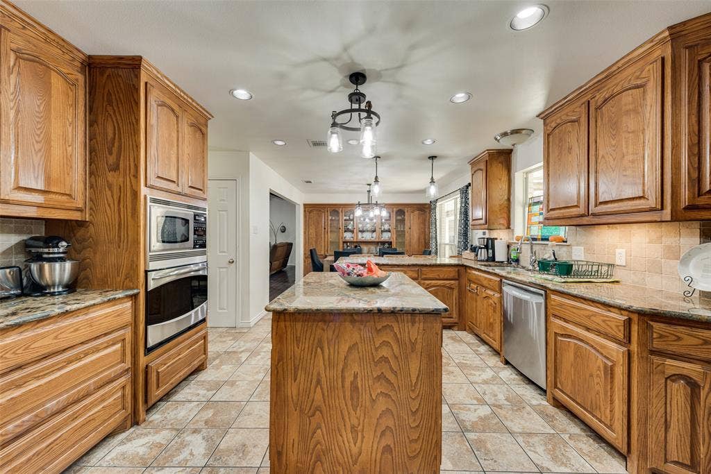 Kitchen featuring wood cabinetry, stone countertops, central island, stainless steel built-in double oven, and tile flooring