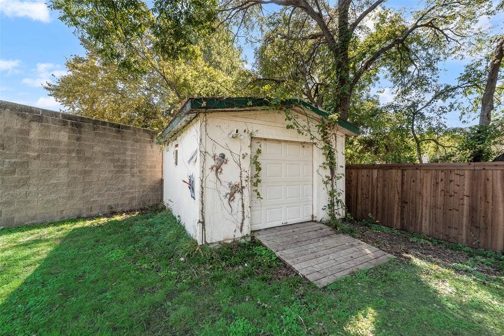 Detached structure featuring a sectional garage door, wood-plank ramp, and concrete block perimeter wall, enclosed by a wood privacy fence