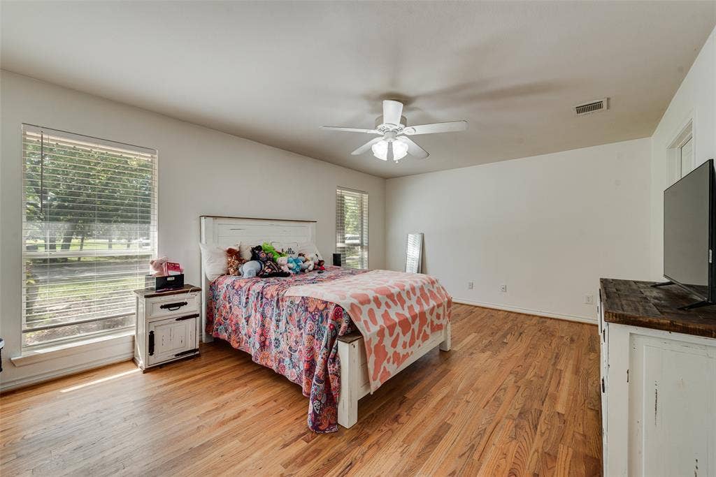 Room featuring wood-finish flooring, dual windows, and a ceiling-mounted light fixture with fan