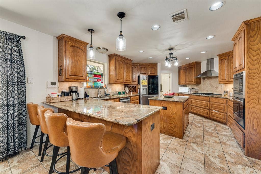 Kitchen featuring raised-panel wood cabinetry, stone countertops, a center island, stone tile flooring, and a stainless steel range hood
