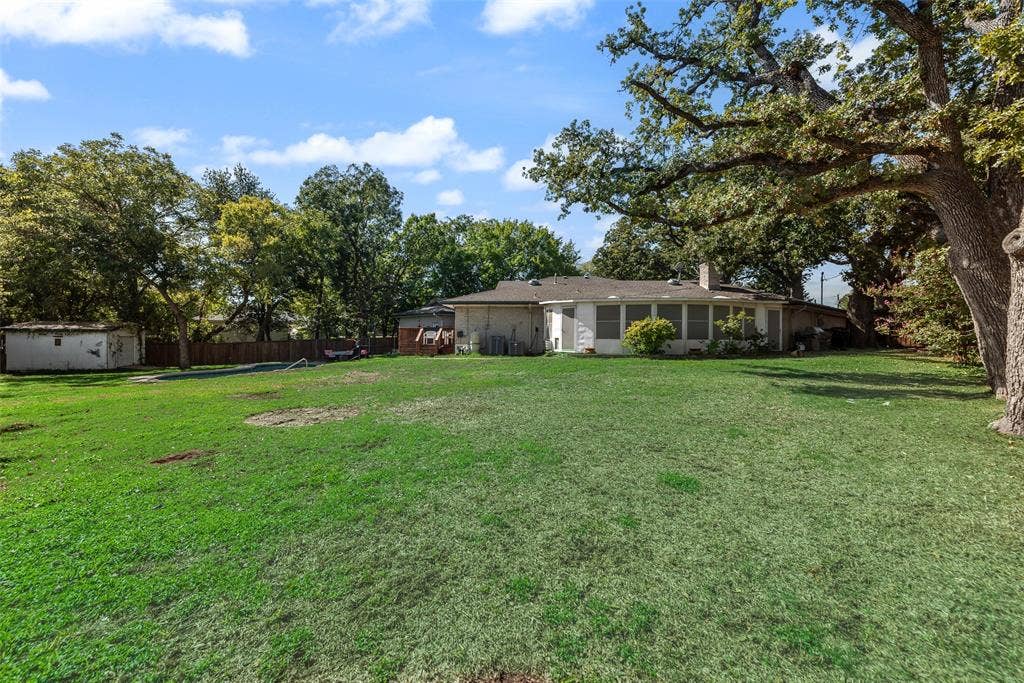 Expansive backyard featuring mature trees, a grass lawn, a detached storage structure, and a fenced perimeter