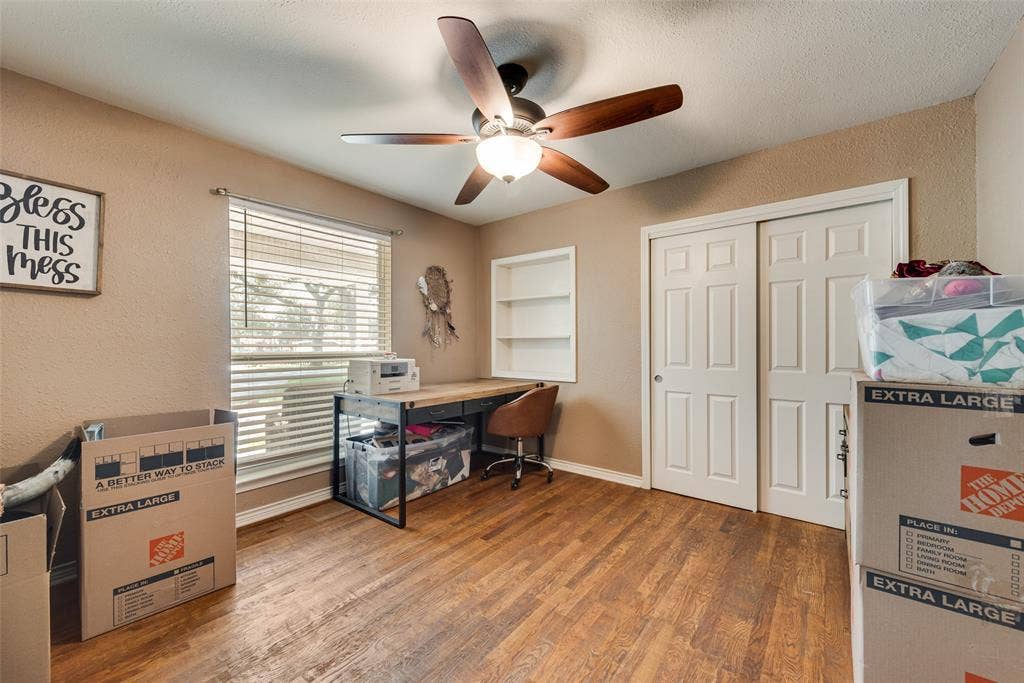 Room featuring wood-finish flooring, a five-blade ceiling fan with integrated light fixture, built-in recessed shelving, and a double-door sliding closet