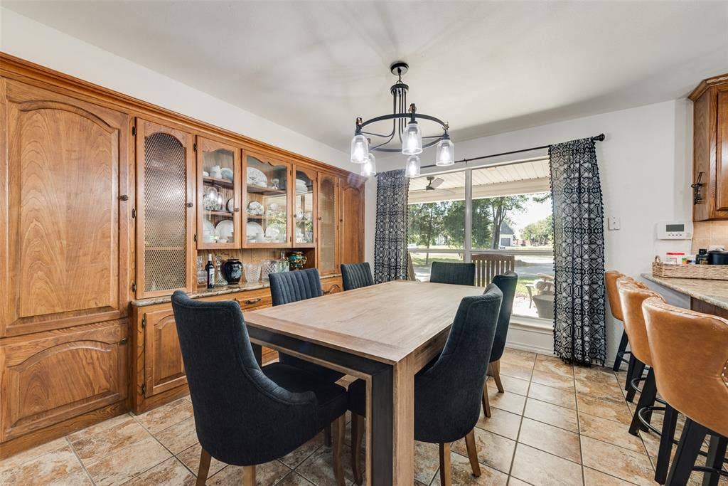 Built-in floor-to-ceiling wood cabinetry with glass-front display sections, stone countertops, tile flooring, and a multi-light chandelier