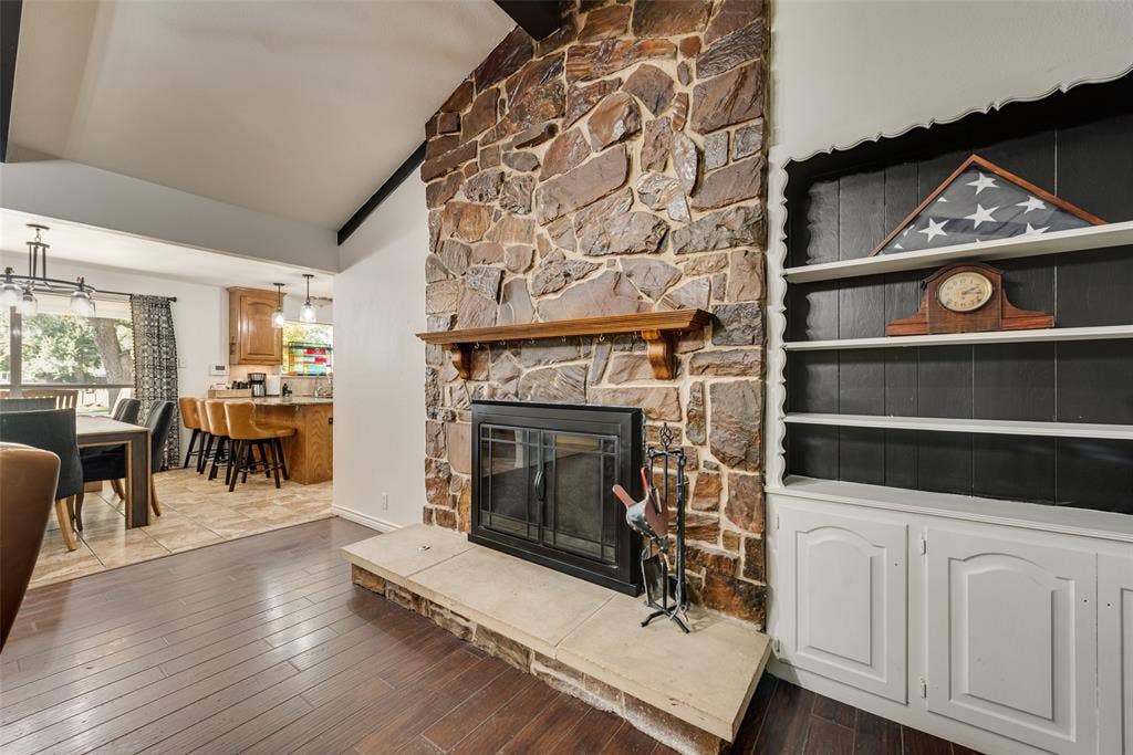 Floor-to-ceiling natural stone fireplace with a wood mantel, raised hearth, and vaulted ceiling, complemented by built-in white cabinetry with open shelving and wood-finish flooring