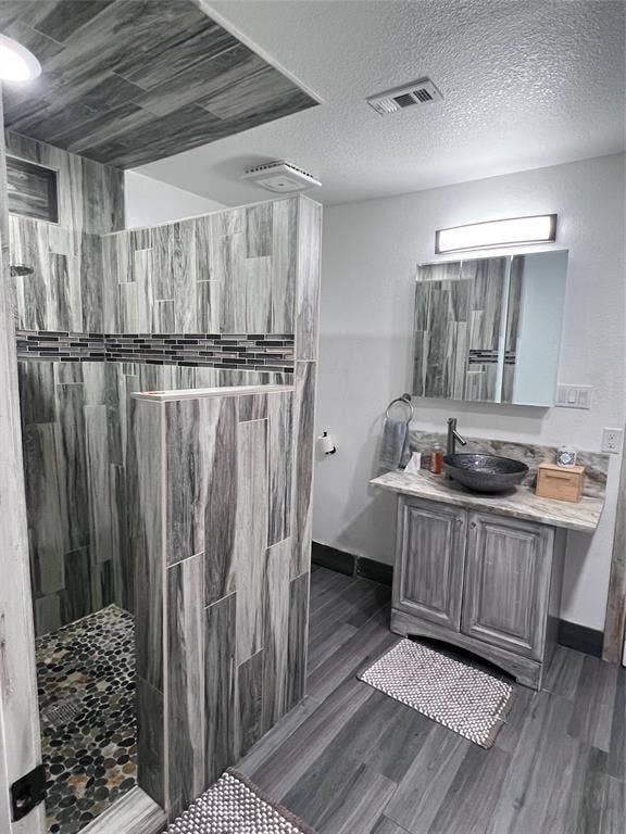 201 Darien Drive, Mesquite, TX 75149 Walk-in shower with stone-tile flooring and vertical-pattern tile surround, vanity with decorative stone-finish countertop, vessel sink, and wall-mounted vanity lighting