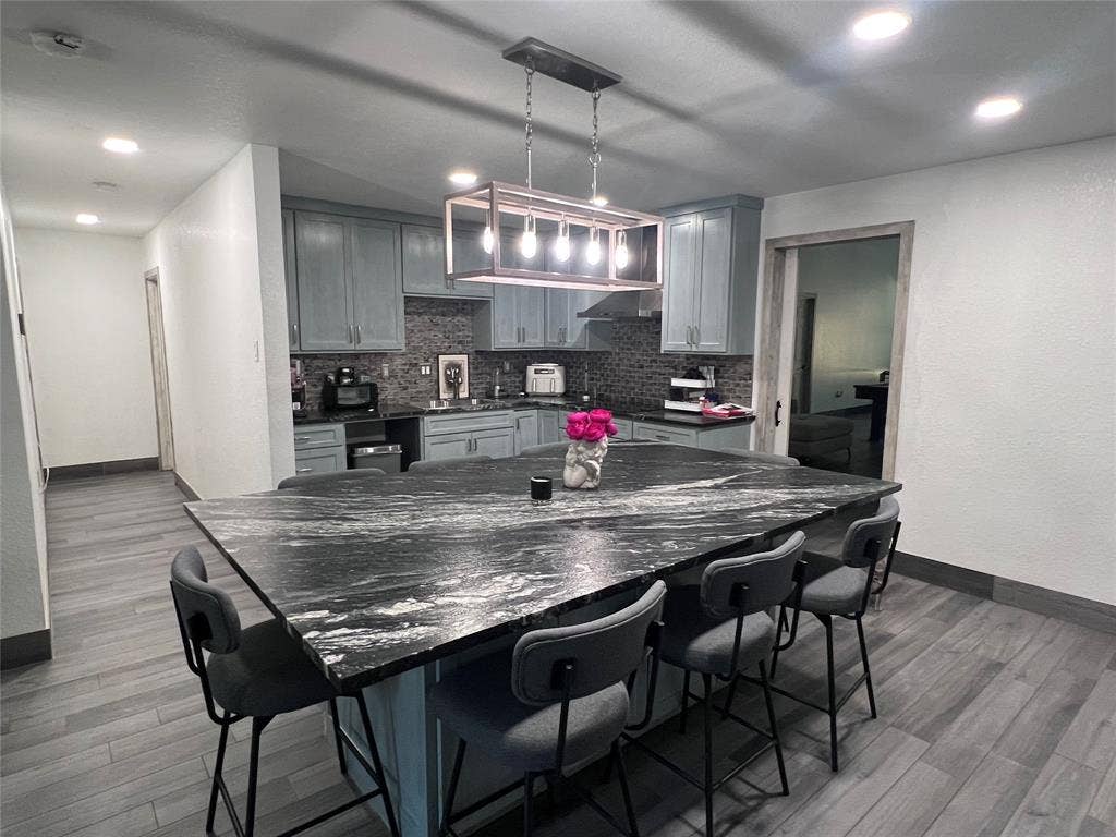 201 Darien Drive, Mesquite, TX 75149 Kitchen featuring a substantial stone-top island, custom cabinetry, tiled backsplash, wood-finish flooring, and a rectangular metal-frame pendant light