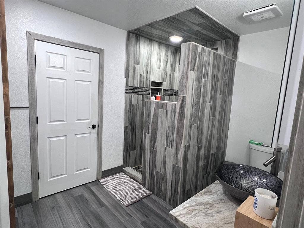 201 Darien Drive, Mesquite, TX 75149 Walk-in shower with vertical wood-finish tile and recessed shelving, stone-finish countertop, vessel sink, and wood-finish flooring