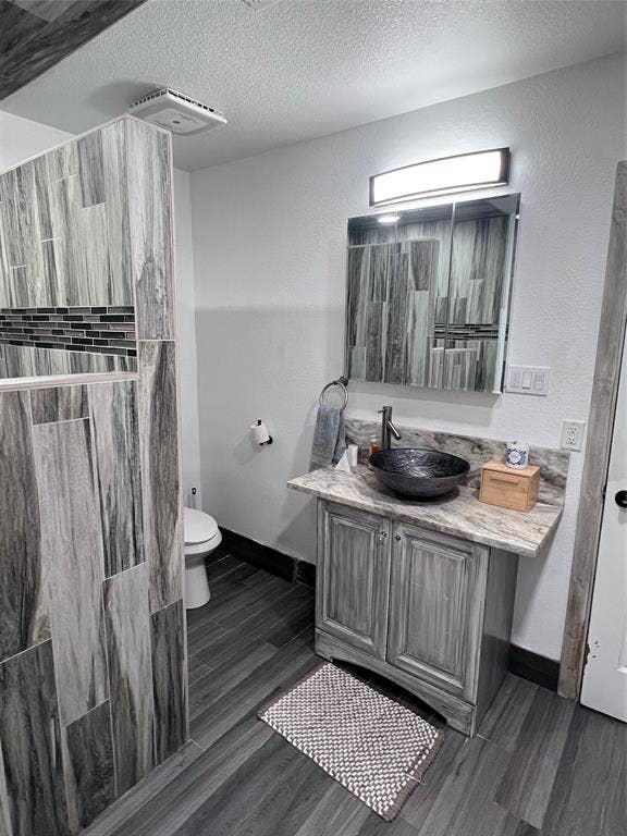 201 Darien Drive, Mesquite, TX 75149 Vanity featuring a stone-finish countertop, vessel sink, and metallic faucet, complemented by wood-finish flooring and a tiled partition wall with decorative mosaic inlay