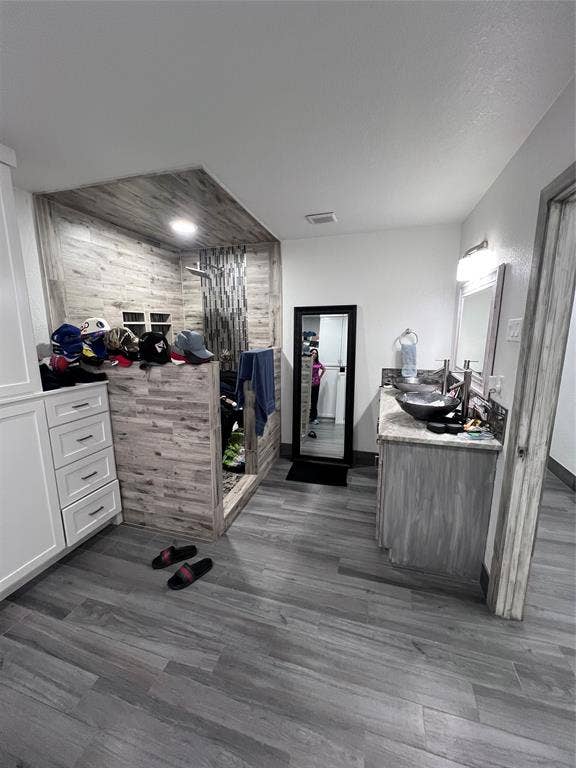 201 Darien Drive, Mesquite, TX 75149 Custom vanity with dual vessel sinks and stone-finish countertop, wood-finish flooring throughout, and a walk-in shower featuring wood-finish tile surround and built-in shelving