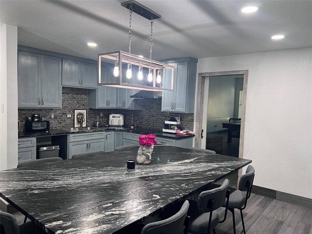 201 Darien Drive, Mesquite, TX 75149 Kitchen featuring a large island with a stone countertop, cabinetry with light blue finish, rectangular pendant light fixture, stone-style backsplash, and wood-finish flooring