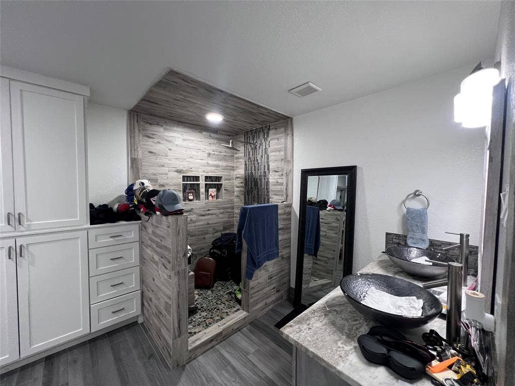 201 Darien Drive, Mesquite, TX 75149 Double vanity featuring stone-patterned countertops, dual vessel sinks with metallic fixtures, full-height white cabinetry with drawer storage, and a walk-in shower with wood-finish wall tile and stone flooring