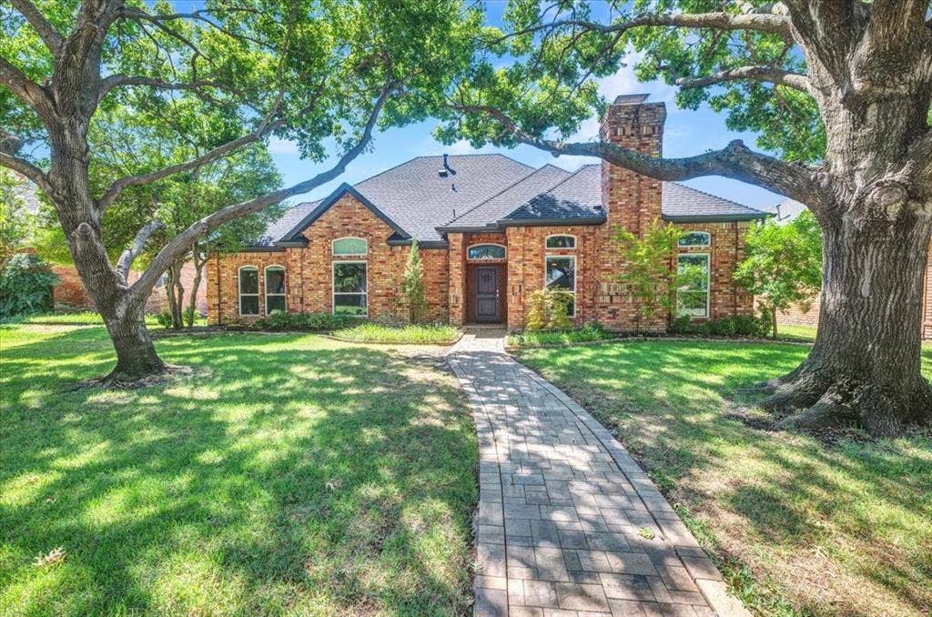 5208 Streamwood Lane, Plano, TX 75093 Brick exterior with a prominent chimney, arched windows, and a paved stone walkway set within a landscape featuring mature trees