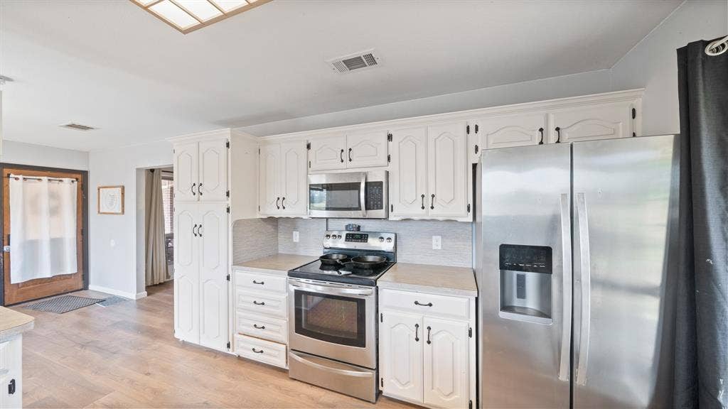 8935 Bluebonnet Drive, Scurry, TX 75158 Kitchen featuring painted cabinetry, stainless steel appliances, neutral countertops, and wood-finish flooring