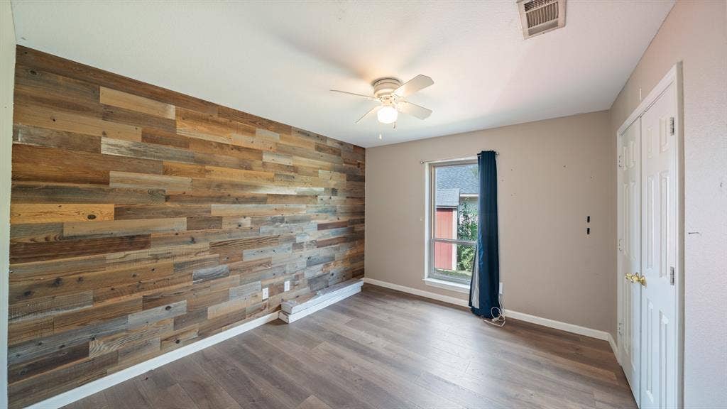 8935 Bluebonnet Drive, Scurry, TX 75158 Wood-plank accent wall featuring varied natural textures, wood-finish flooring, ceiling fan with integrated lighting, and white six-panel closet doors