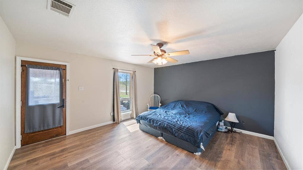 8935 Bluebonnet Drive, Scurry, TX 75158 Wood-finish flooring, dark grey accent wall, ceiling fan with integrated lighting, and wooden exterior door with glass insert