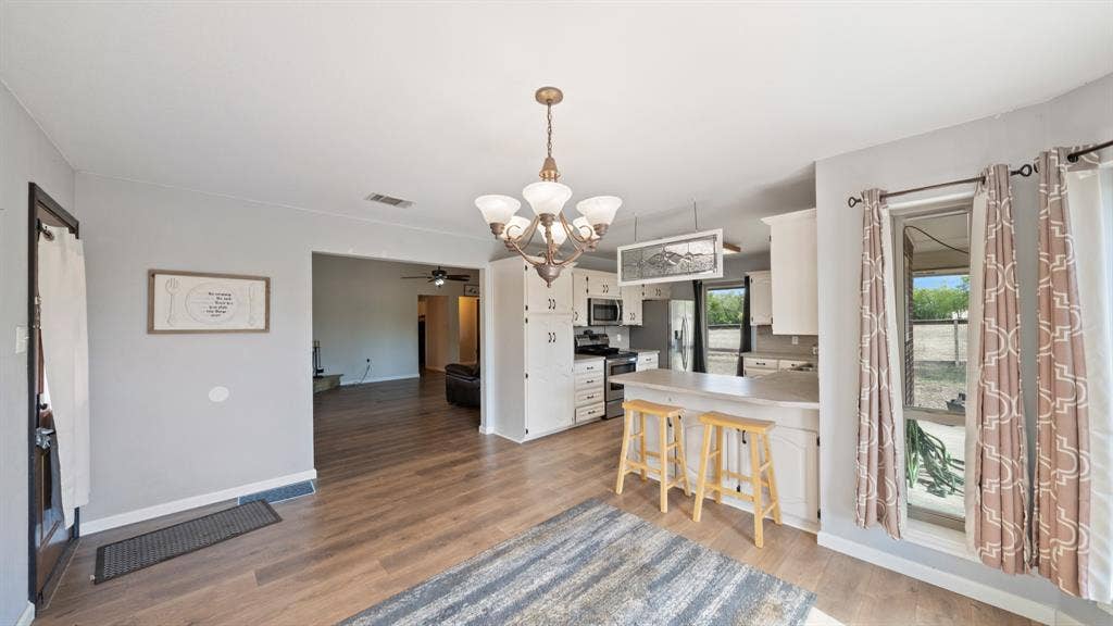 8935 Bluebonnet Drive, Scurry, TX 75158 Kitchen area featuring white cabinetry, a breakfast bar, wood-finish flooring, and a multi-arm chandelier