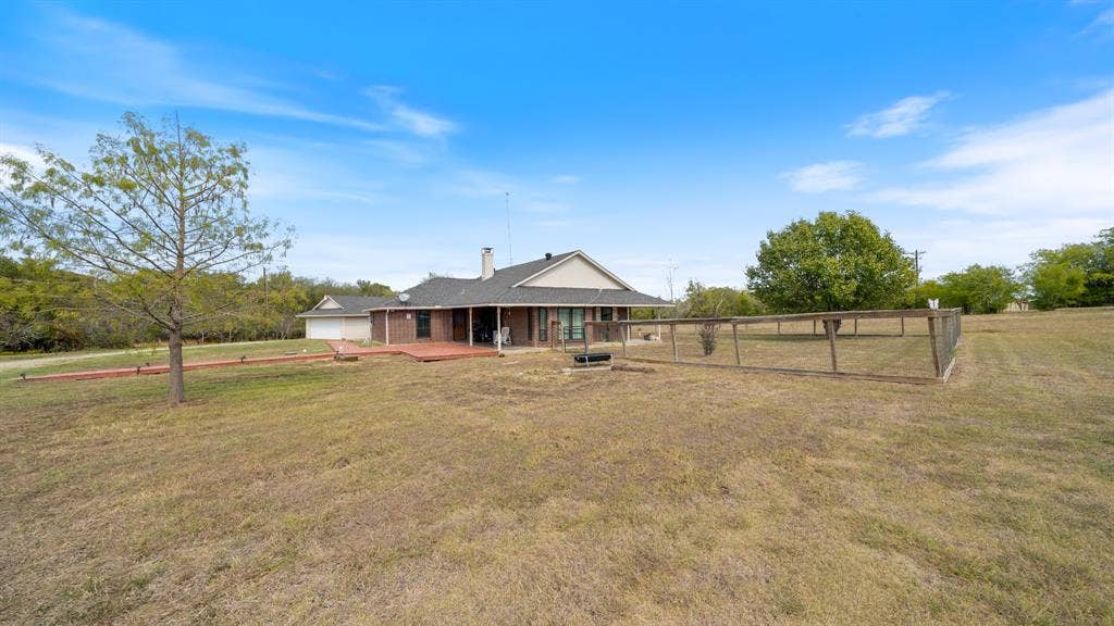 8935 Bluebonnet Drive, Scurry, TX 75158 Single-story brick exterior residence featuring a covered patio, attached garage, and perimeter wire fencing on an expansive acreage lot