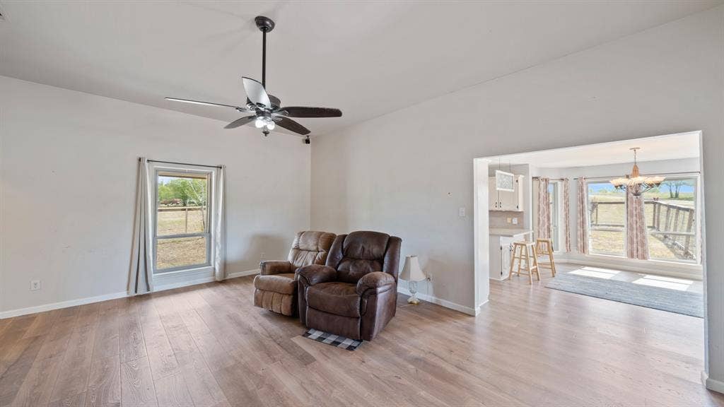 8935 Bluebonnet Drive, Scurry, TX 75158 Living area featuring wood-finish flooring, a ceiling fan with integrated lighting, and neutral wall tones, highlighted by natural light through large windows