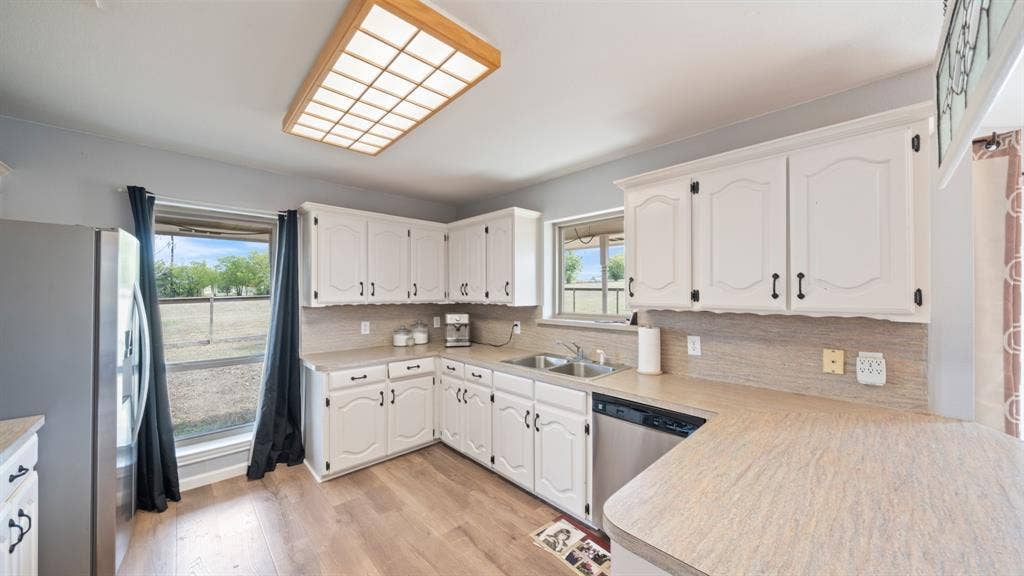 8935 Bluebonnet Drive, Scurry, TX 75158 Kitchen featuring white cabinetry with dark hardware, laminate countertops, stainless steel dual-basin sink, stainless steel dishwasher, and wood-finish flooring