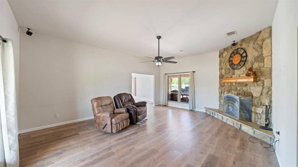 8935 Bluebonnet Drive, Scurry, TX 75158 Living area featuring wood-finish flooring, a floor-to-ceiling stone fireplace with a raised hearth, a wooden mantel, and a ceiling fan