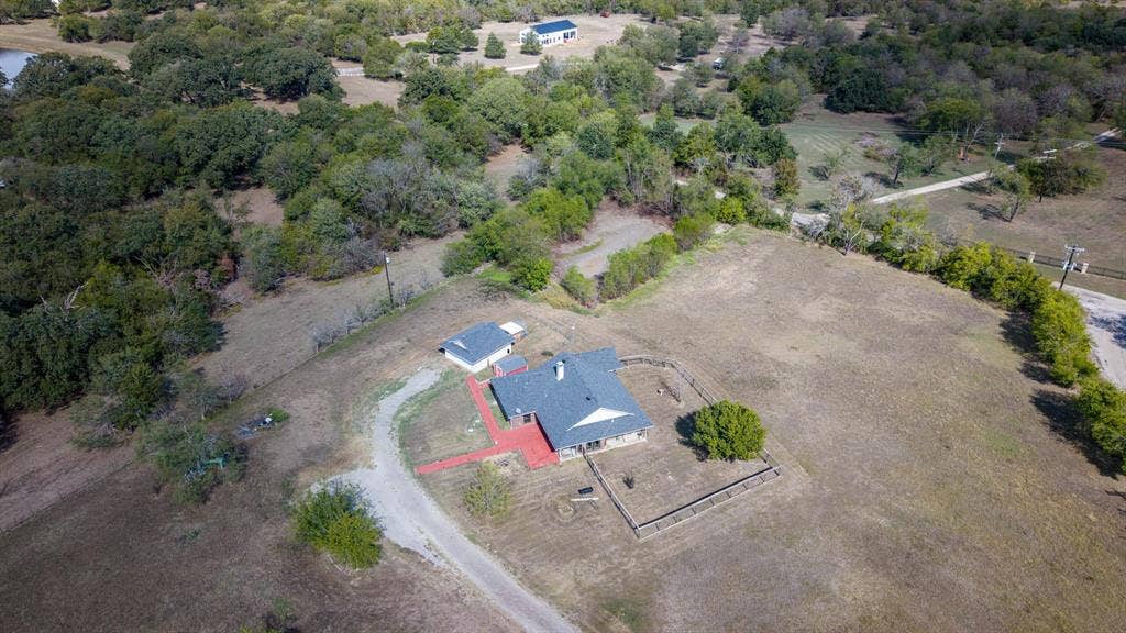 8935 Bluebonnet Drive, Scurry, TX 75158 Aerial perspective of a sprawling property featuring a detached structure, gravel driveway, segmented perimeter fencing, and mature trees across an expansive lot