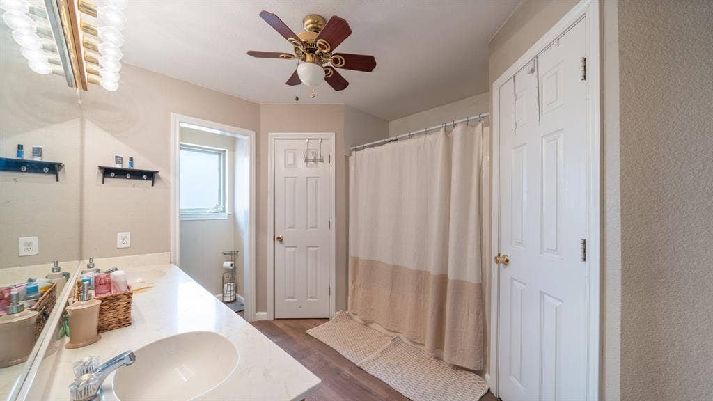 8935 Bluebonnet Drive, Scurry, TX 75158 Bathroom featuring a vanity with integrated sink, expansive wall-to-wall mirror, multi-bulb overhead lighting, ceiling fan, and wood-finish flooring