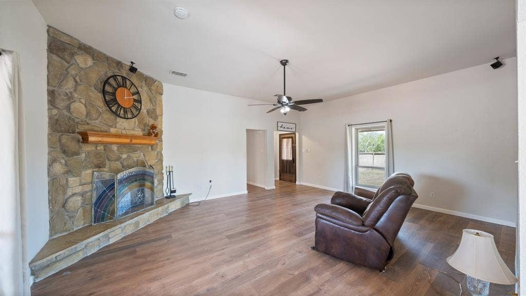 8935 Bluebonnet Drive, Scurry, TX 75158 Floor-to-ceiling stone fireplace with a prominent hearth and wooden mantel, wood-finish flooring, high ceilings, and a ceiling fan