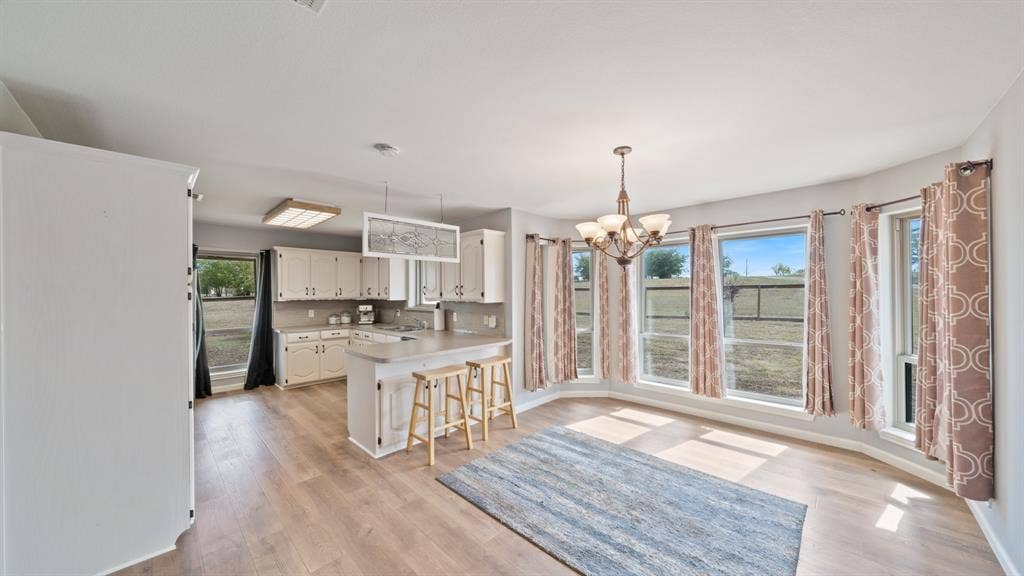 8935 Bluebonnet Drive, Scurry, TX 75158 Kitchen featuring white cabinetry, wood-finish flooring, a breakfast bar, and large windows providing natural light