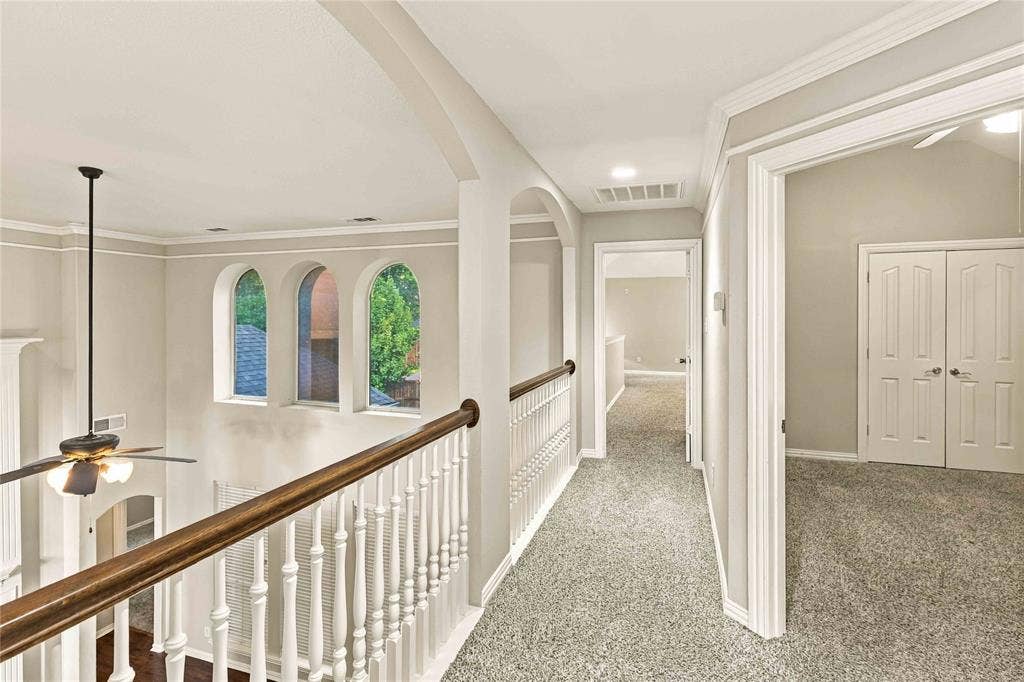 Interior balcony featuring decorative arched wall cutouts, wood-topped railing with white balusters, recessed lighting, and crown molding
