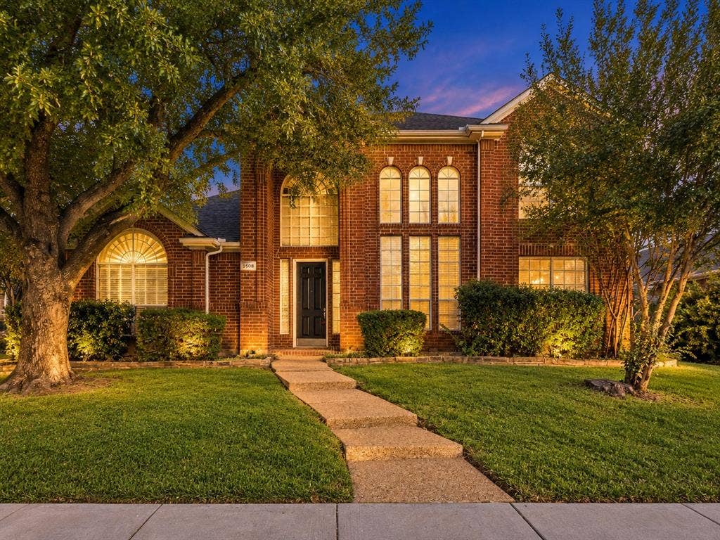 Traditional red brick exterior featuring a multi-gabled roofline, arched window detailing, and a concrete paver walkway leading to the front entry