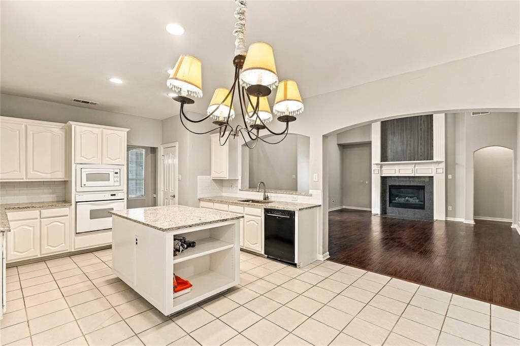 Kitchen featuring white cabinetry, stone countertops, a center island, and built-in appliances, including a fireplace with a decorative mantel in the area beyond