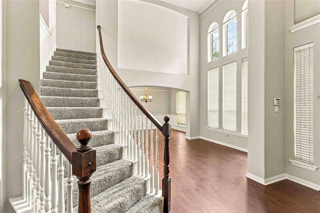 Grand foyer featuring high ceilings, a sweeping staircase with a polished wood handrail, wood-finish flooring, and arched floor-to-ceiling windows
