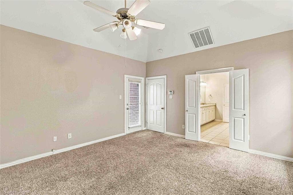 Vaulted ceilings with a central multi-blade ceiling fan, neutral wall tones, carpeted flooring, and double doors opening to a secondary space