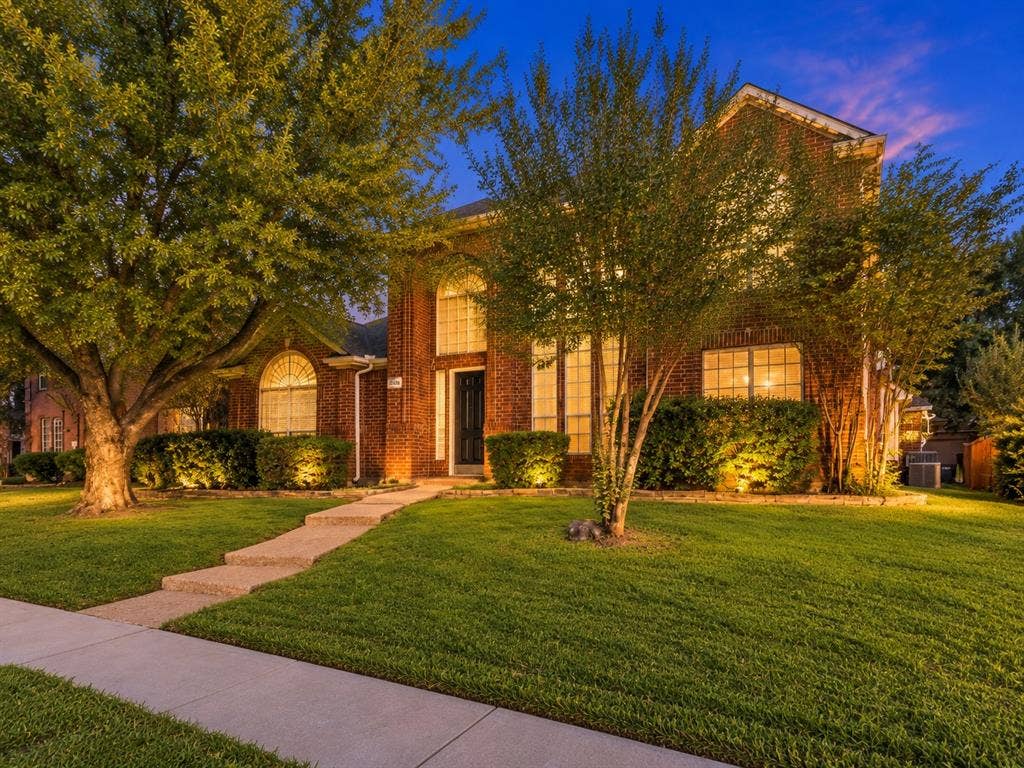 Two-story brick exterior featuring an arched entryway, decorative arched windows, a stone-paved walkway, and established landscaping