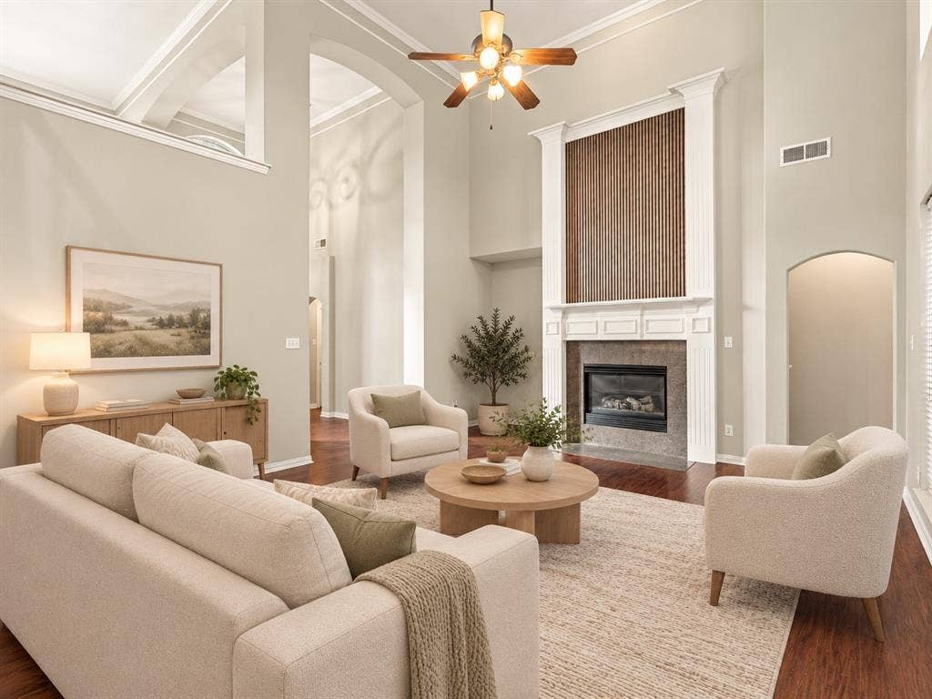 High-ceilinged living area featuring a fireplace with a stone surround, vertical wood-slat detailing, white crown molding, and wood-finish flooring
