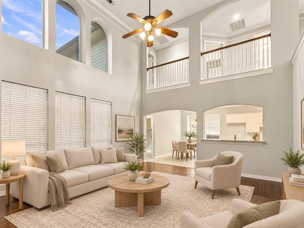 Double-height living area featuring arched windows, wood-finish flooring, a ceiling fan with integrated lighting, and an overlooking interior balcony with a white railing