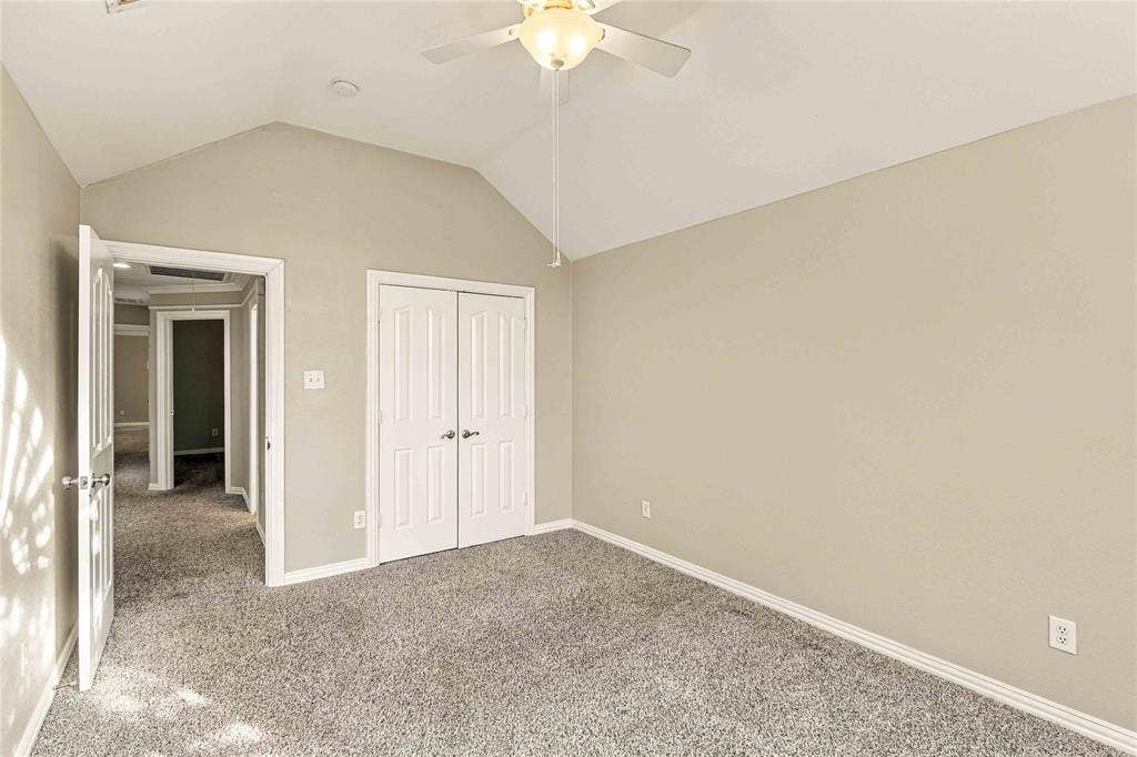 Vaulted ceilings featuring a central ceiling fan, neutral wall finishes, and double-door closet cabinetry