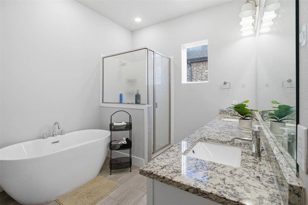 1408 Rockcliff Street, Plano, TX 75093 Freestanding soaking tub, glass-enclosed shower, dual-sink vanity with stone countertop, tile flooring, and oversized vanity mirror