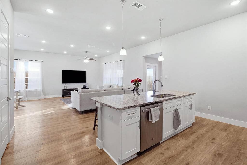 1408 Rockcliff Street, Plano, TX 75093 Kitchen island with stone-surface countertop, stainless steel dishwasher, white cabinetry, wood-finish flooring, and recessed ceiling lighting