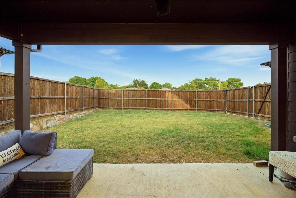 1408 Rockcliff Street, Plano, TX 75093 Covered patio featuring a concrete floor, stone-accented wood perimeter fencing, and an expansive lawn