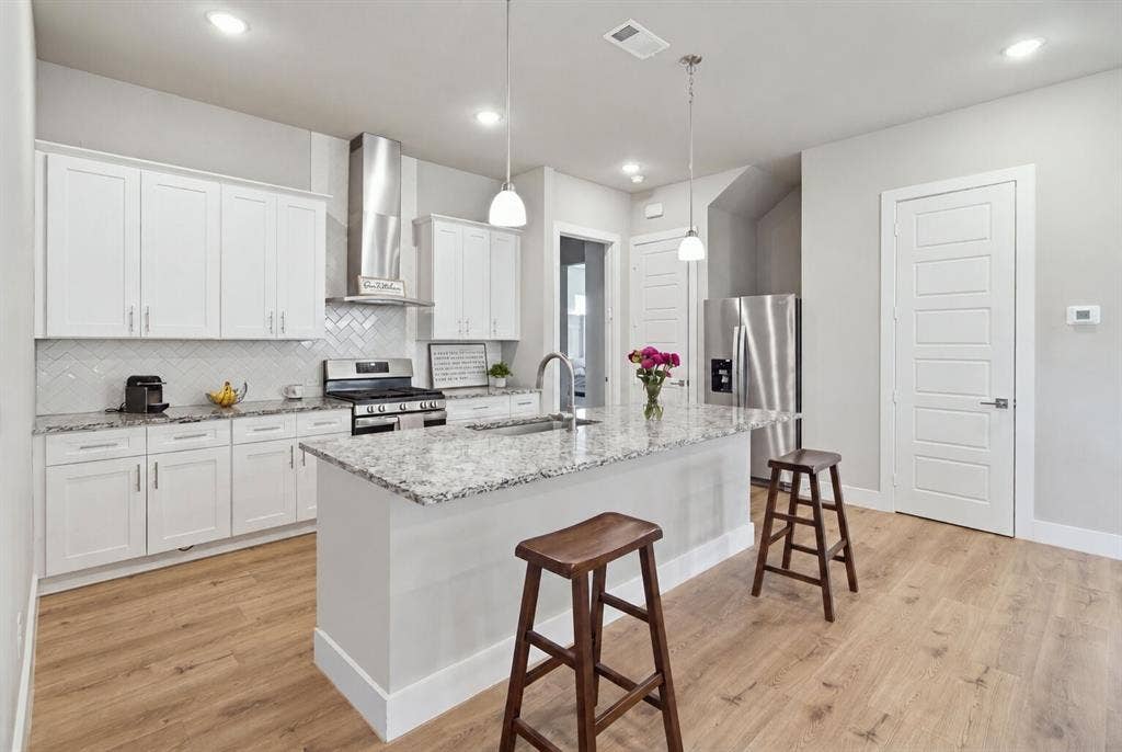 1408 Rockcliff Street, Plano, TX 75093 Kitchen featuring white cabinetry, stone-surface countertops, chevron-patterned backsplash, stainless steel appliances, and wood-finish flooring