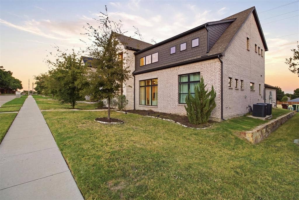 1408 Rockcliff Street, Plano, TX 75093 Two-story exterior featuring light-toned brick masonry, dark shingle siding, expansive picture windows, and a stone retaining wall