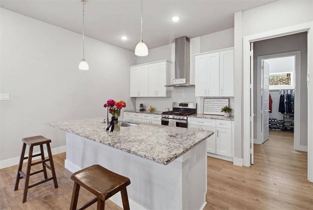 1408 Rockcliff Street, Plano, TX 75093 Kitchen featuring white cabinetry, stone countertops, stainless steel range with chimney-style hood, pendant lighting, and wood-finish flooring