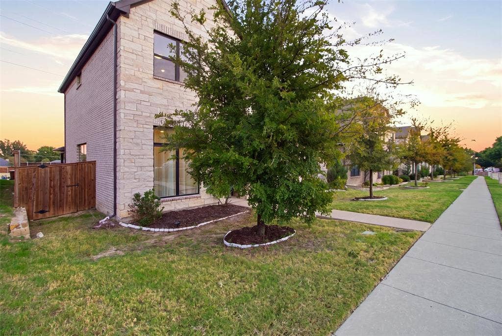 1408 Rockcliff Street, Plano, TX 75093 Exterior featuring light-toned stone masonry, dark-framed windows, and a wood privacy fence